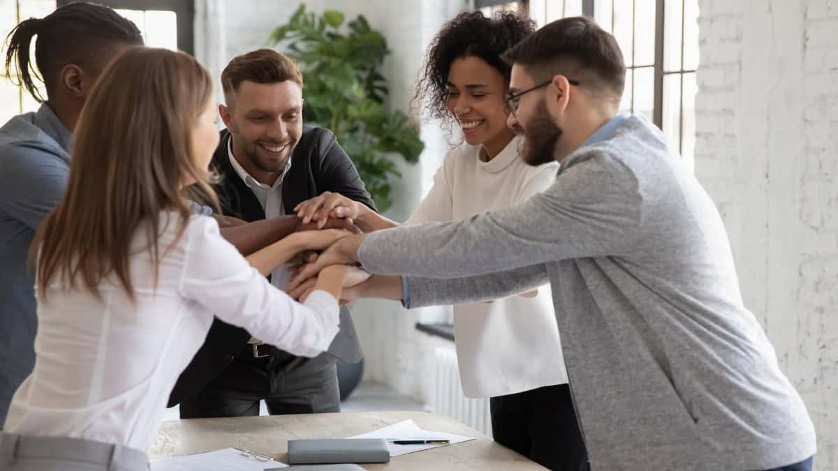 Group of employee engagement gathering around a table as a team with their hands in the center